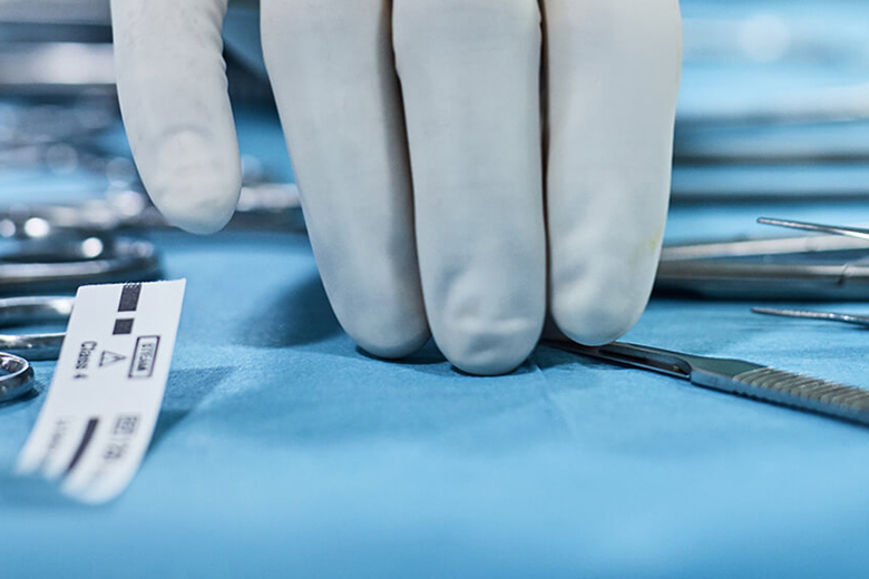 surgical tools on table with gloved hand reaching for them