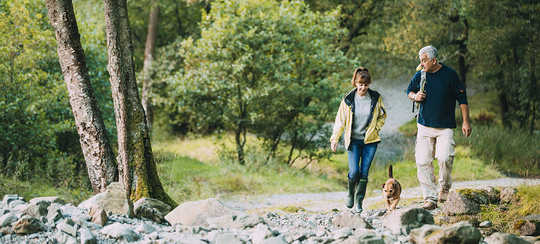 Senior couple are hiking through the Lake District together with their pet dog.